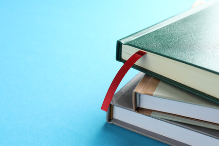 Book with red ribbon bookmark and colorful ones on light blue background, closeup. Space for textの写真素材