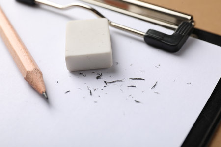 Eraser, pencil, scraps and clipboard on brown background, closeupの写真素材