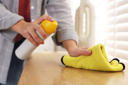 Woman using cleaning product while polishing wooden table with rag indoors, closeup