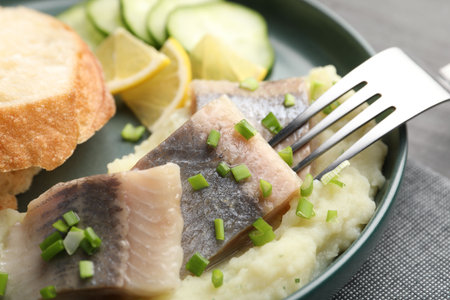 Pieces of delicious herring, mashed potato, cucumber slices and bread served on black table, closeupの写真素材