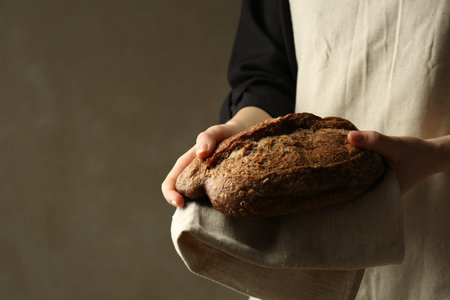 Woman with fresh loaf of bread on gray background, closeup