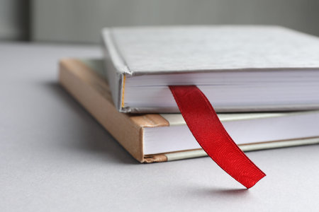 Book with red ribbon bookmark and colorful one on light table against gray background, closeupの写真素材