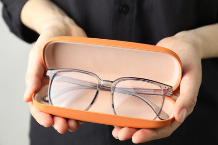 Woman holding case with stylish glasses on light background, closeupの写真素材