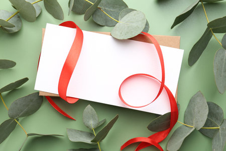 Blank card, ribbon and eucalyptus branches on light green background, flat layの写真素材