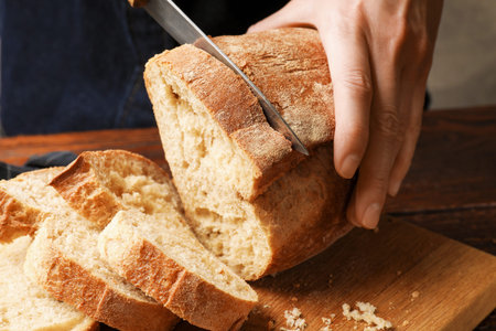 Woman cutting fresh bread at wooden table, closeup