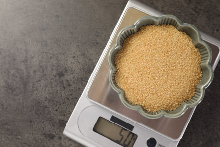 Digital kitchen scale with bowl of brown sugar on grey table, top view. Space for textの写真素材