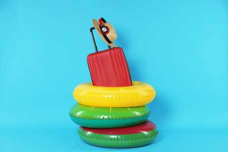 Colorful inflatable rings, suitcase, straw hat and headphones on light blue background