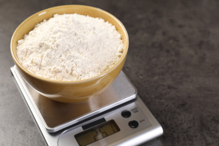 Digital kitchen scale with bowl of flour on gray table, closeup. Space for textの写真素材