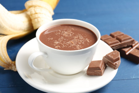 Tasty chocolate milk in cup, pieces and banana on blue wooden table, closeupの写真素材
