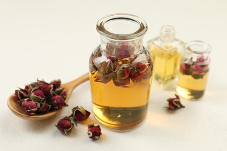 Open perfume bottles with aromatic essential oils and dried roses on white table, closeup