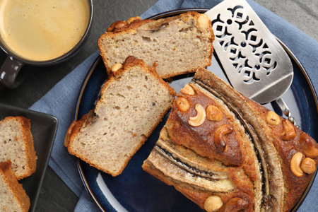 Cut banana bread with nuts, server and coffee on black table, flat lay
