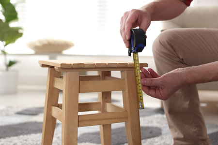 Man measuring wooden stool with tape indoors, closeupの写真素材