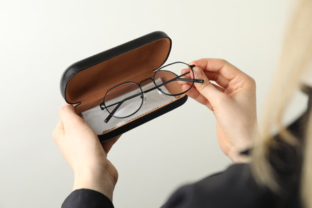 Woman holding case with stylish glasses and cleaning cloth on light background, closeup