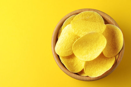 Tasty potato chips in bowl on yellow background, top view. Space for textの写真素材