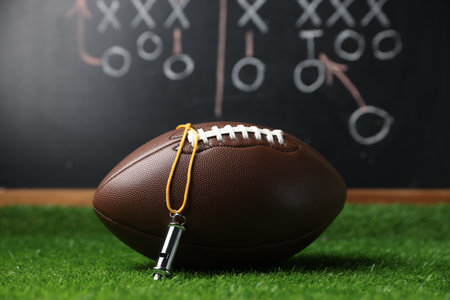 American football ball and whistle on green grass against chalkboard with game schemeの写真素材