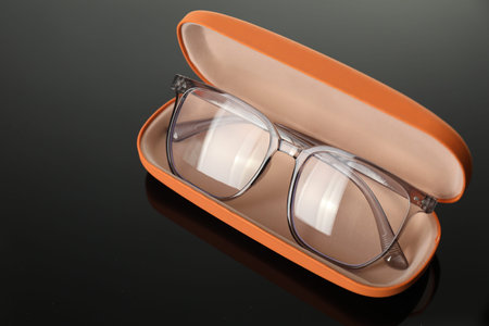Stylish glasses in case on grey mirror surface, closeup