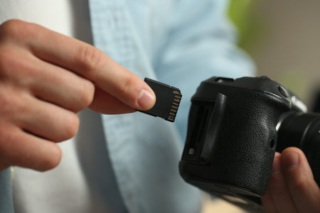 Man inserting SD memory card into photo camera indoors, closeup