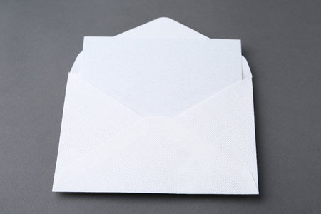 Blank greeting card in paper envelope on dark gray background, closeup