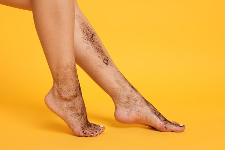 Woman with body scrub on her legs against orange background, closeupの写真素材