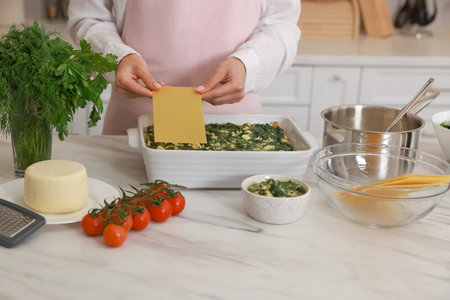 Woman making spinach lasagna at marble table indoors, closeupの写真素材