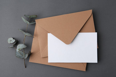 Blank greeting card, envelopes and eucalyptus leaves on gray background, flat layの写真素材