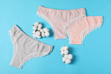 Women's underwear. Beautiful panties and cotton flowers on light blue background, flat layの写真素材