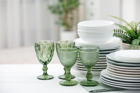 Clean glasses, plates and green houseplant on white wooden table indoors, space for textの写真素材