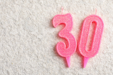 30th birthday. Number shaped candles on light textured background, top view. Space for textの写真素材