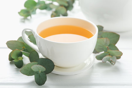 Aromatic tea in cup and eucalyptus branches on white wooden table, closeupの写真素材