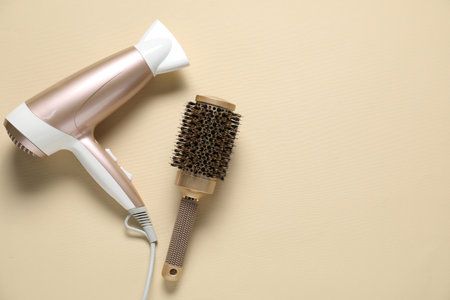 Round brush and dryer on beige background, flat lay. Space for textの写真素材
