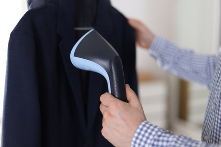 Man steaming jacket with stand steamer indoors, closeupの写真素材