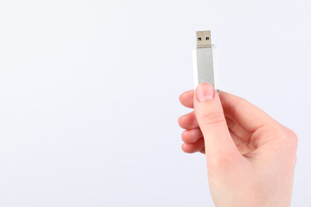 Man with modern flash drive on light gray background, closeup. Space for text