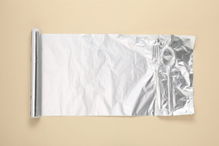 Roll of aluminum foil on beige background, top view