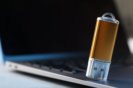 Modern flash drive and laptop on table, closeup. Space for text