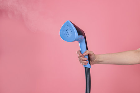 Woman with clothes steamer on pink background, closeup. Space for textの写真素材