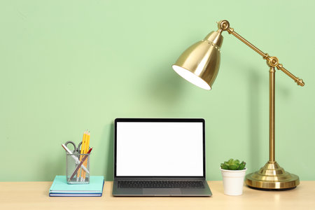 Stylish workplace with modern laptop on wooden desk near light green wallの写真素材