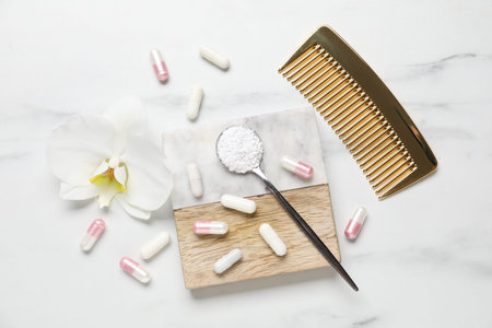 Collagen capsules, powder, comb and flower on white marble table, flat layの写真素材