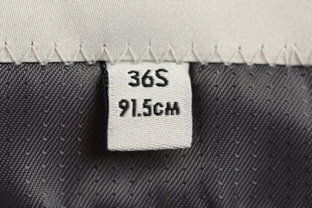 Clothing label on black garment as background, closeup