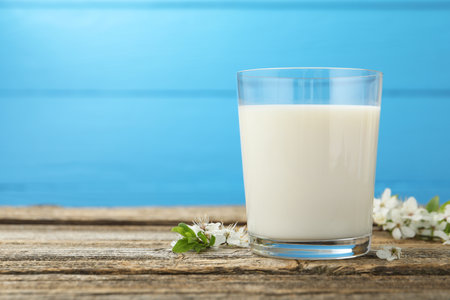 Fresh milk in glass and blossoms on wooden table against light blue background, closeup. Space for textの写真素材