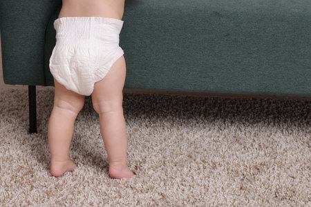 Cute little baby standing near sofa at home, closeup. Space for textの写真素材