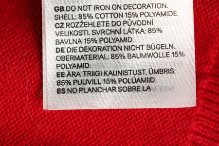 Clothing label in different languages on red garment, closeup