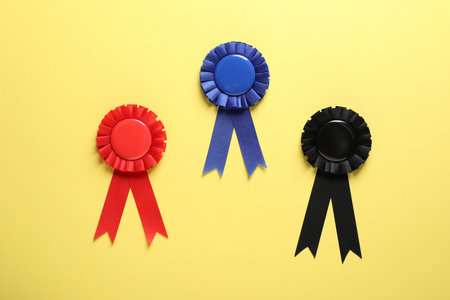 Different award ribbons on yellow background, flat lay