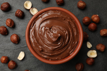 Tasty chocolate hazelnut spread and nuts on black table, flat layの写真素材