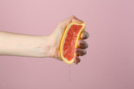 Woman squeezing grapefruit on pink background, closeupの写真素材