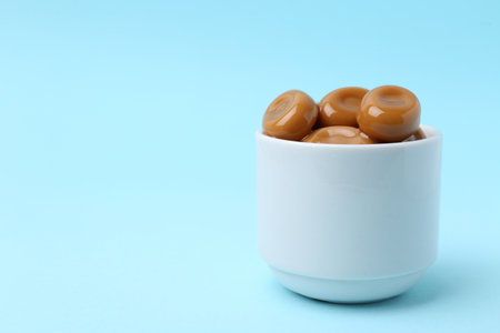 Sweet caramel candies on light blue background, closeup. Space for textの写真素材