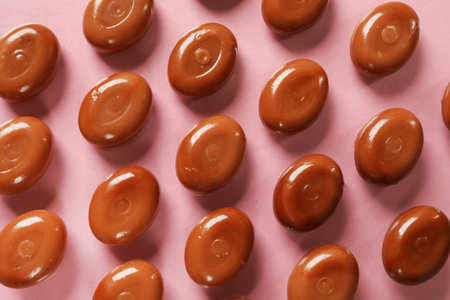 Many tasty caramel candies on light pink background, flat layの写真素材