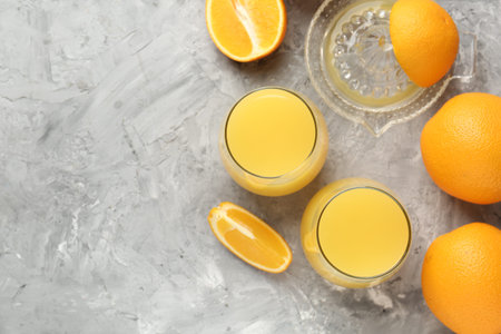 Orange juice in glasses, fresh fruits and juicer on gray table, flat lay. Space for text