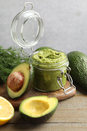 Tasty avocado dip in glass jar, dill and fruits on wooden table, closeup