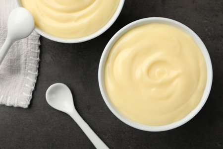 Tasty vanilla pudding and spoon on black table, flat lay