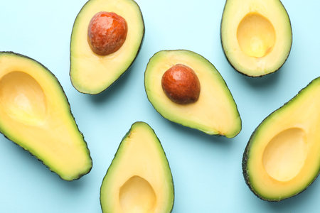 Halves of fresh avocados on light blue background, flat lay
